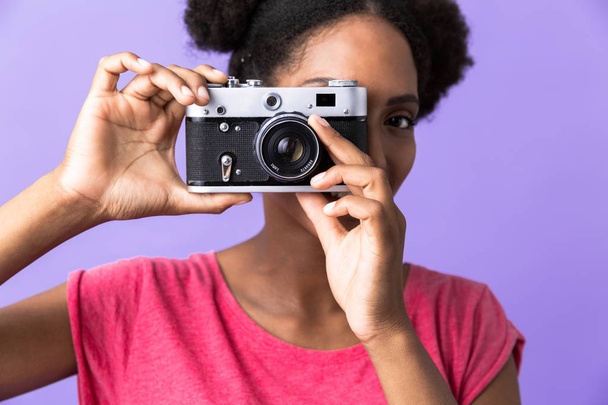 Photo of young african american woman smiling and photographing on retro camera isolated over violet background - Φωτογραφία, εικόνα