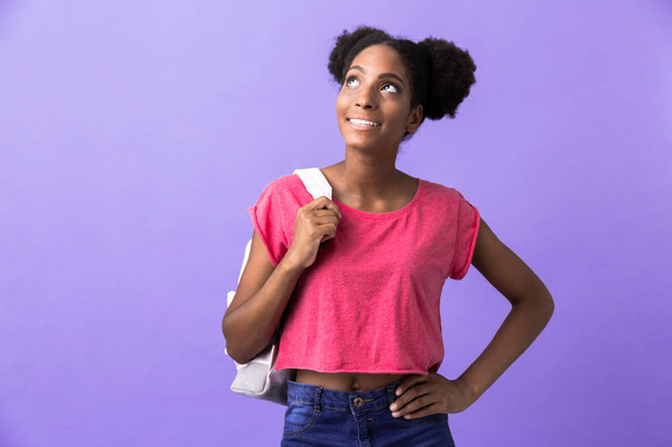 Photo of candid african american woman student wearing backpack smiling and looking upward isolated over violet background - Foto, Bild
