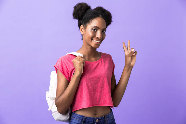 Photo of brunette african american woman student wearing backpack showing peace sign isolated over violet background - Φωτογραφία, εικόνα