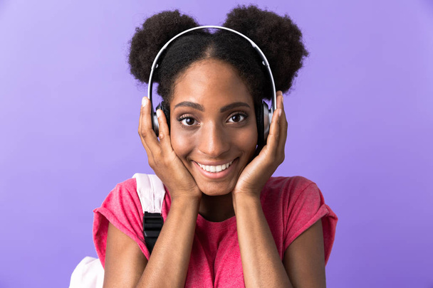 Фото гарна жінка студент посміхаючись в білі навушники, ізольовані над фіолетовий фону - Фото, зображення
