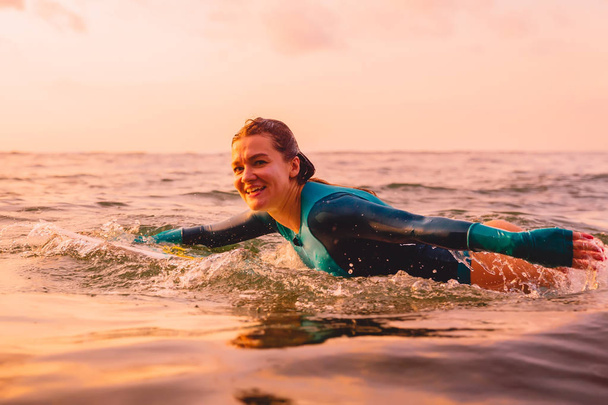 attraktive Surferin Frau auf einem Surfbrett schwimmen im Meer. Surfen bei Sonnenuntergang - Foto, Bild