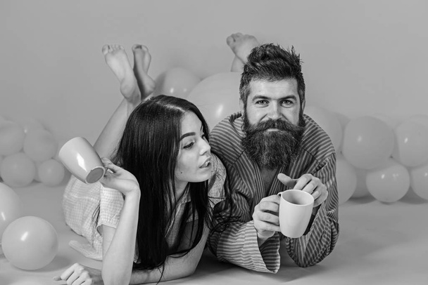 Couple relax in morning with coffee. Couple in love drink coffee in bed. Man and woman in domestic clothes, pajamas. Perfect morning and love concept. Guy with beard drink coffee with dreamy lady - Fotó, kép