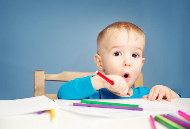 Little child drawing on the paper. Boy sitting on the chair at table with pencils - Foto, imagen
