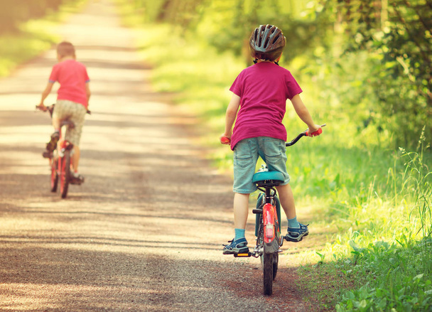 children riding on a bicycles at asphalt road in the park in summer - Fotoğraf, Görsel