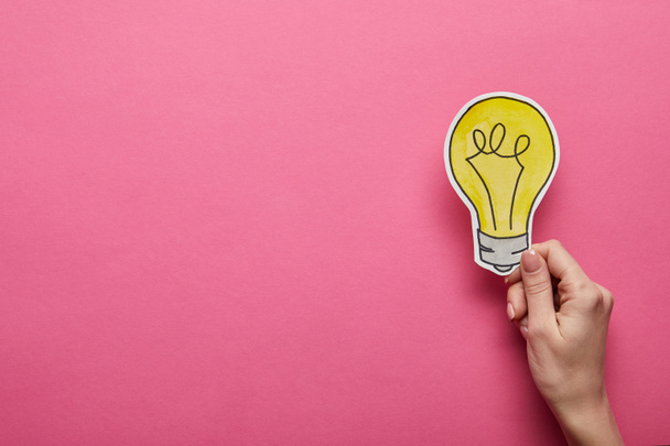 top view of hand holding yellow light bulb on pink background - Photo, Image