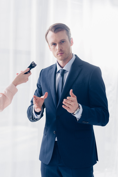 cropped image of handsome businessman giving interview to journalist with voice recorder and looking at camera in office - Fotoğraf, Görsel