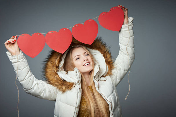 Girl in winter coat with hood on holding four hearts garland - Foto, immagini