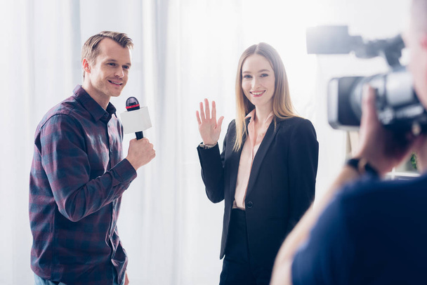 mulher de negócios bonita sorridente no terno que dá a entrevista ao jornalista e acenando a mão no escritório
 - Foto, Imagem