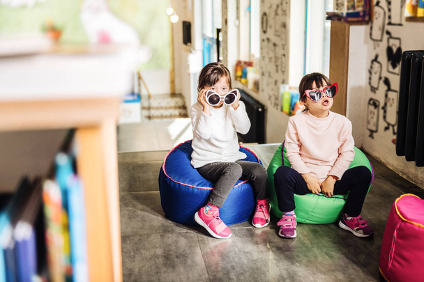 Funny sunglasses. Two twins wearing bright pink sneakers and funny sunglasses playing together - Фото, изображение