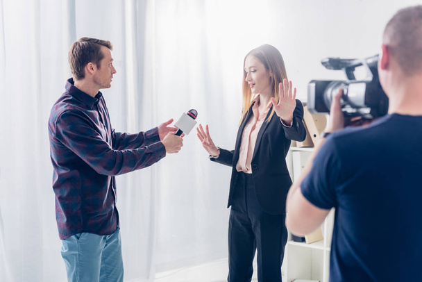 beautiful businesswoman in suit rejecting giving interview to journalist and showing stop sing to cameraman in office - Photo, image