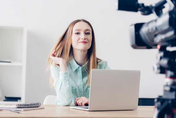 sorridente attraente video blogger femminile registrazione vlog in ufficio e guardando la fotocamera
 - Foto, immagini