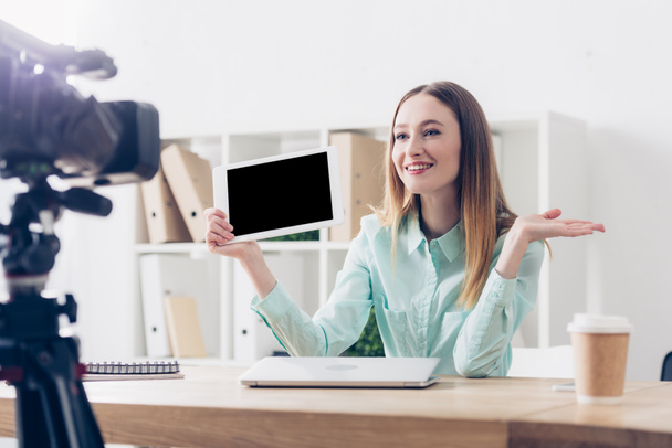 smiling attractive female video blogger recording vlog and holding tablet with blank screen in office - Foto, Imagem