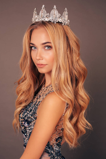 fashion studio photo of gorgeous beautiful woman, winner of beauty competition, with long blond hair in luxurious evening dress with crown on her head - Fotoğraf, Görsel