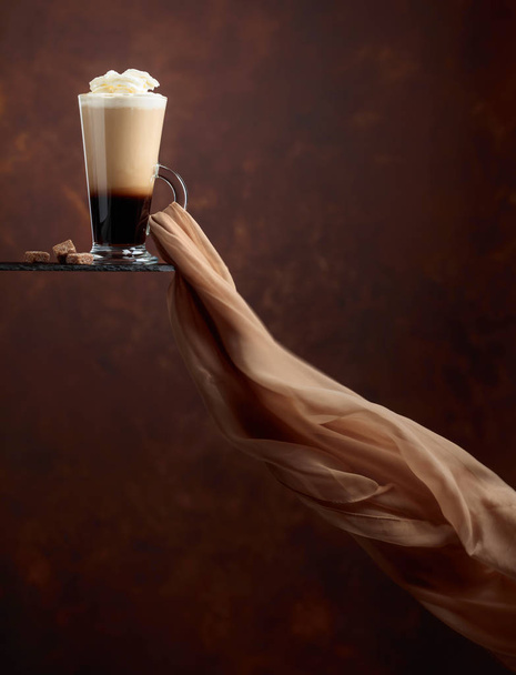 Picie kawy lub koktajl ze śmietaną i kawałki brązowego cukru na brązowym tle. Rozwija się w szalik szyfonu wiatr. Miejsce dla tekstu. - Zdjęcie, obraz