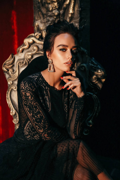 fashion interior photo of gorgeous sexy woman with dark hair in luxurious lace dress posing in theater interior, sitting in antic style chair - Foto, Imagen