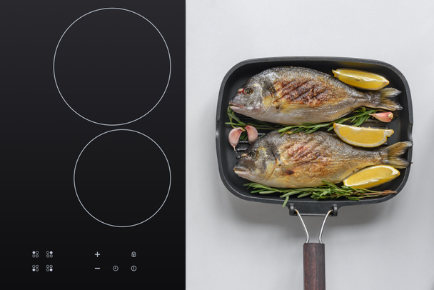 вид на вкусную жареную рыбу Дорадо с розмарином, лимоном и чесноком
 - Фото, изображение