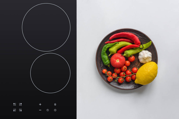 top view of fresh vegetables on plate and electric stove - Photo, Image