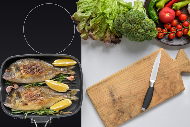 top view of wooden cutting board with knife, fresh vegetables and fried dorado fish - Foto, afbeelding