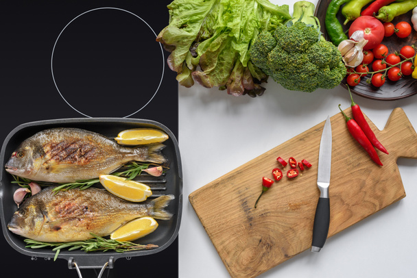 top view of delicious fried fish on electric stove and fresh vegetables with wooden cutting board and knife - Foto, afbeelding