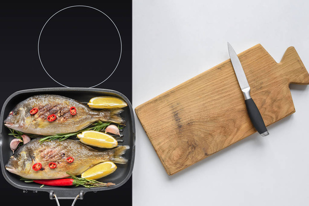 top view of delicious fried fish on electric stove and wooden cutting board with knife - Foto, imagen