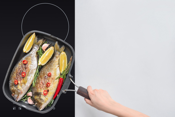 cropped shot of person cooking tasty fried fish with lemon, rosemary and cherry tomatoes - Photo, Image