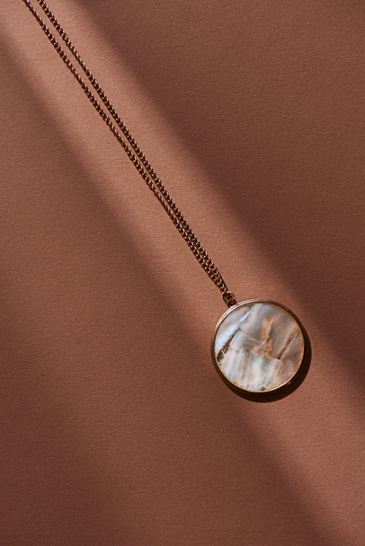 top view of beautiful round locket with marble on brown surface with sunlight - Photo, Image