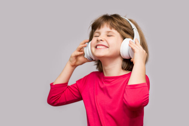 Energy kid girl with headphones listening to music with closed eyes on white background in studio. - Foto, afbeelding