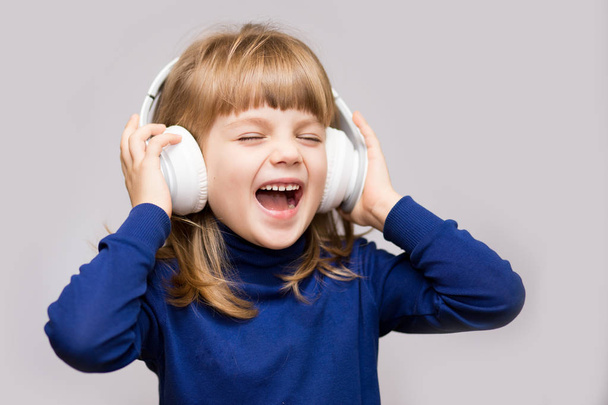 Energy kid girl with headphones listening to music with closed eyes on white background in studio. - Φωτογραφία, εικόνα