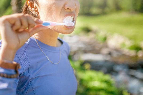 woman brushing teeth at mountain river during hike outdoors. Concept of personal hygiene during travel - 写真・画像