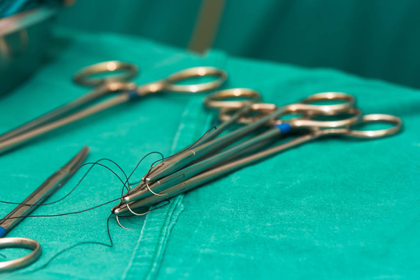 Portaagujas con agujas y suturas y tijeras en la mesa de operaciones en el procedimiento quirúrgico
. - Foto, Imagen