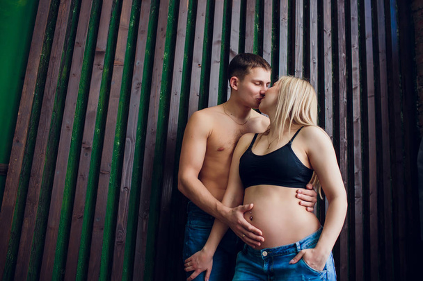 Terhes pár a szerelem a fából készült fal közelében, nevetve, és várakozás-re a baba. Várakozás-re egy csoda, a boldog szülők, család. - Fotó, kép