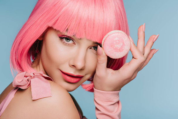 attractive young woman in pink wig posing with macaron isolated on blue - Photo, Image