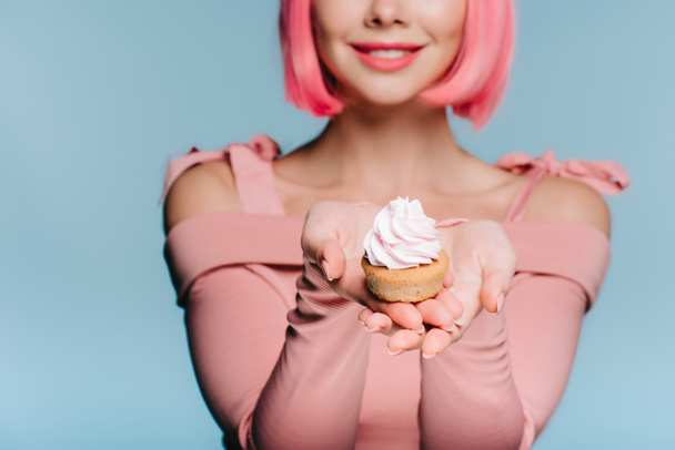 gülümseyen kız mavi izole tatlı cupcake tutarak görünümünü kırpılmış - Fotoğraf, Görsel