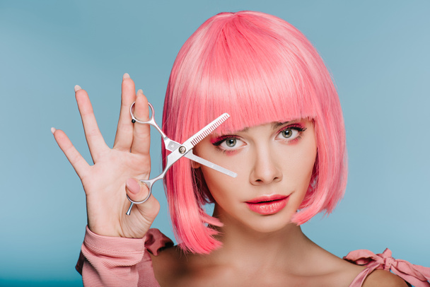 attractive fashionable girl in pink wig posing with scissors isolated on blue - Photo, Image