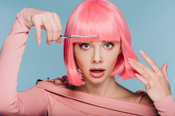 schockiert stilvolles Mädchen schneidet rosa Haare mit Schere isoliert auf blau - Foto, Bild