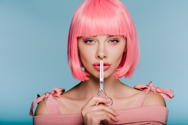 κομψό και αισθησιακό κορίτσι σε ροζ περούκα δείχνει σιωπή σύμβολο με το ψαλίδι που απομονώνονται σε μπλε - Φωτογραφία, εικόνα
