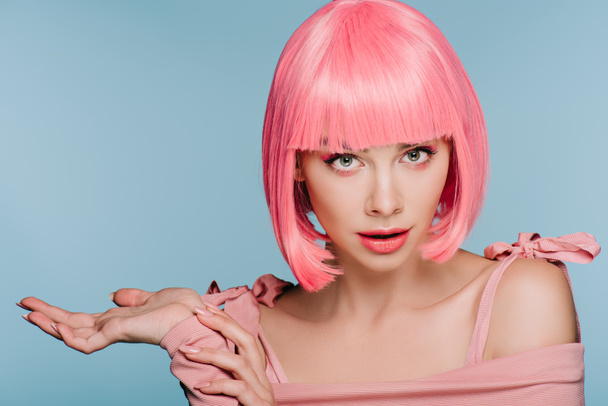 beautiful shocked girl in pink wig posing with shrug gesture isolated on blue - Foto, Bild