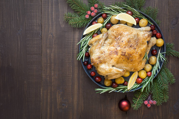 Traditional Christmas roasted chicken with potatoes and rosemary on wooden table. Top view. - Foto, afbeelding