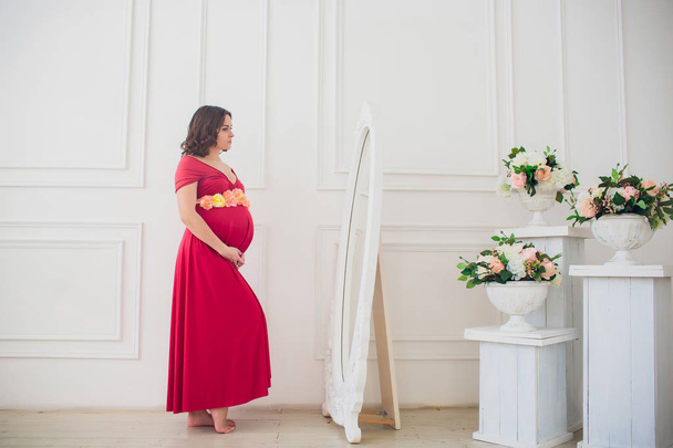 Beautiful pregnant woman looking in mirror in light room - Fotografie, Obrázek