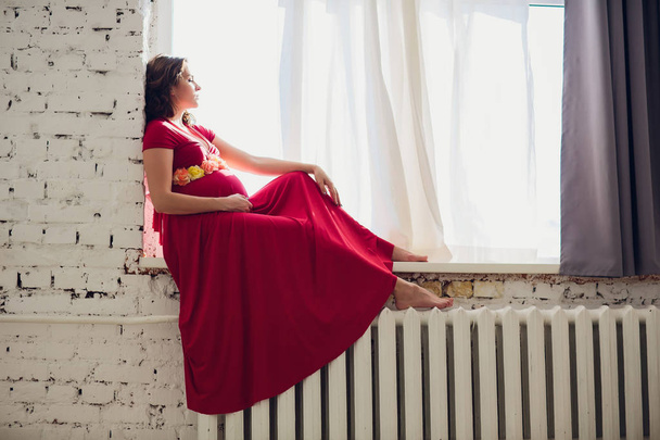 Pregnant woman in a red dress lying on the window - Foto, immagini