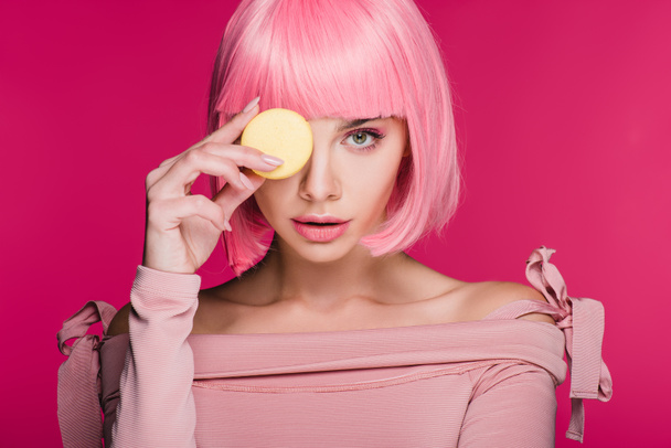 young fashionable woman in pink wig posing with macaron isolated on pink - Foto, immagini