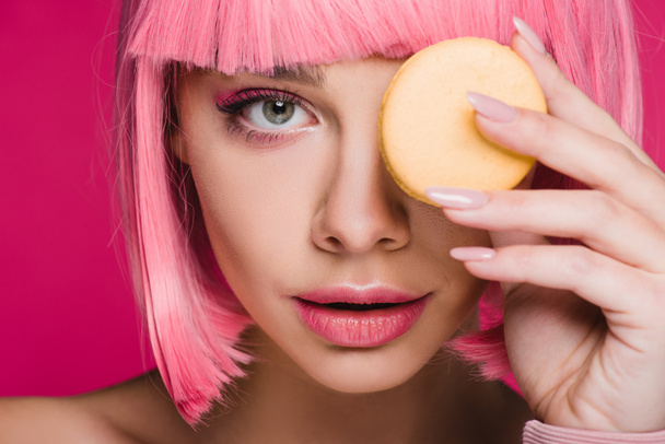 atractiva chica de peluca rosa posando con macaron amarillo aislado en rosa
 - Foto, Imagen