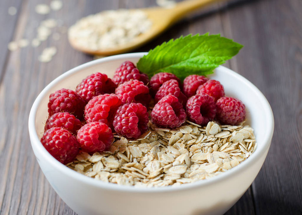 Healthy vegetarian food. Oatmeal with raspberry. Wooden spoon with cereals. Brown wooden background. - 写真・画像