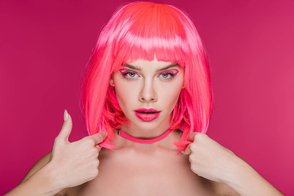schöne junge Frau posiert in neonpinkfarbener Perücke, isoliert auf rosa - Foto, Bild