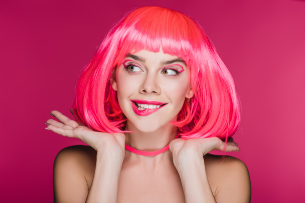 kaunis tyttö puree huuli ja poseeraa neon vaaleanpunainen peruukki, eristetty vaaleanpunainen
 - Valokuva, kuva