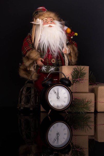 Santa Claus, clock and christmas gifts on a black background with reflection. Copy space. Merry Christmas and Happy New Year, background - Photo, Image