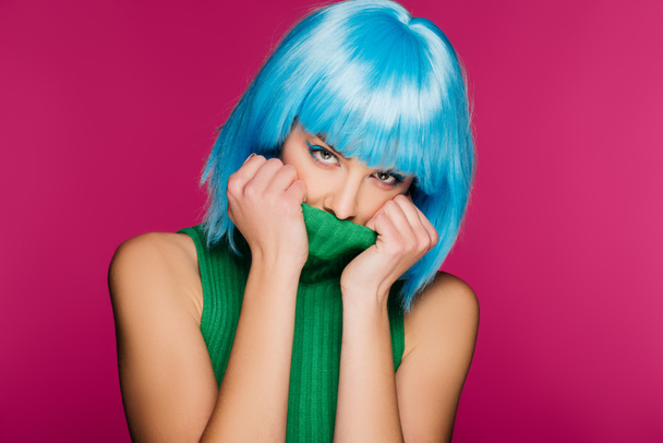 attractive girl with blue hair hiding face in green turtleneck, isolated on pink - Фото, зображення