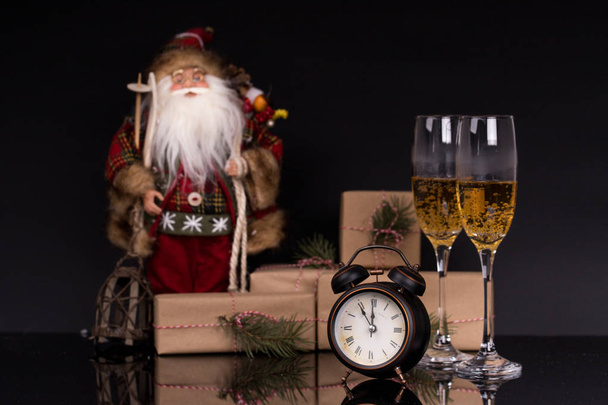 Dos copas de vino con champán, Santa Claus, reloj y regalos de Navidad sobre un fondo negro con reflejo. Copiar espacio. Feliz Navidad y Feliz Año Nuevo, fondo
 - Foto, Imagen