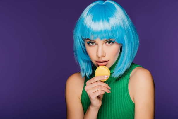 beautiful sensual girl in blue wig posing with sweet tasty macaron isolated on purple - Photo, Image