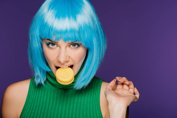 attractive sensual woman in blue wig biting macaron isolated on purple - Photo, Image